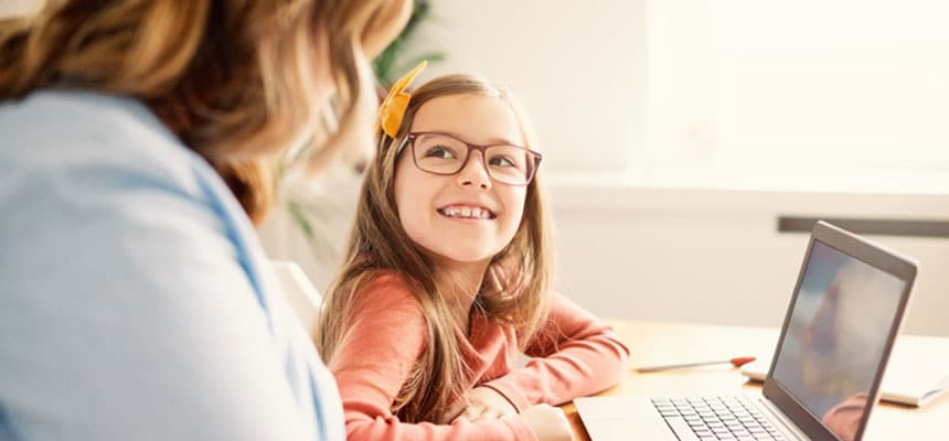 Girl smiling looking at mother reading laptop.