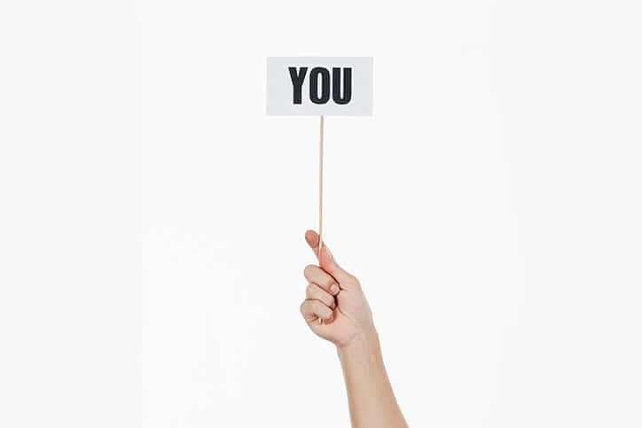 A sign reading "you" is held aloft by a white female hand.
